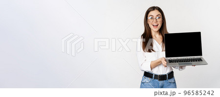 Young woman in glasses showing laptop screen, demonstrating promo on computer, website or store, standing over white background 96585242