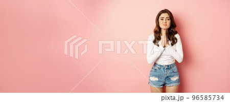 Please. Young stylish girl begging, holding hands in pray, need help, pleading, supplicating, standing against pink background 96585734