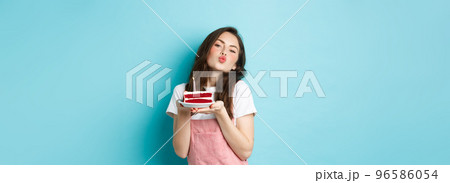 Holidays and celebration. Cute silly girl making wish on birthday cake, making kissing face, celebrating b-day, standing cheerful against blue background 96586054
