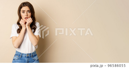 Portrait of scared woman trembling, watching smth scary and looking insecure timid, posing against beige background Portrait of scared woman trembling, watching smth scary and looking insecure timid, posing against beige background 96586055