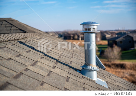 side view of a Galvanized metal chimney exhaust on asphalt roof with a rain cap side view of a Galvanized metal chimney exhaust on asphalt roof with a rain cap 96587135