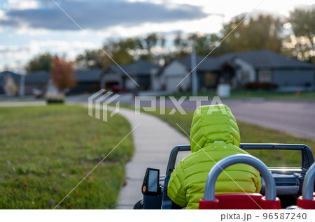 Caucasian boy driving an electric toy car down a sidewalk. Caucasian boy driving an electric toy car down a sidewalk. 96587240