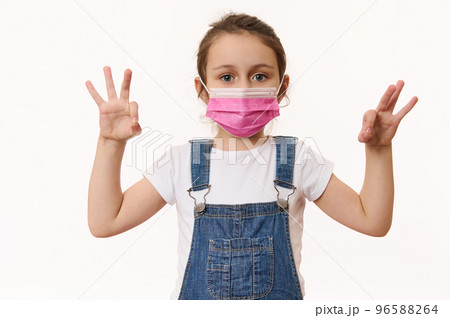 Adorable Caucasian little girl wearing pink protective medical mask, gestures with hands, shows OK signs, looks at camera, isolated over white background. Free space. Pediatrics. Health care. Medicine Adorable Caucasian little girl wearing pink protective medical mask, gestures with hands, shows OK signs, looks at camera, isolated over white background. Free space. Pediatrics. Health care. Medicine 96588264