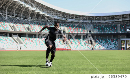 African American man playing football on the stadium field. A man runs with a soccer ball across the field. 96589479