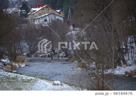 Small old house on hill visible from the bridge over the river flowing down in covered in snow valley Small old house on hill visible from the bridge over the river flowing down in covered in snow valley 96589676