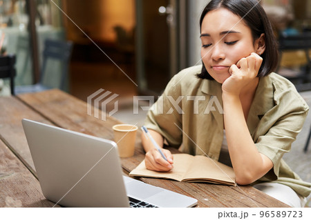 Portrait of young korean girl making notes, listening online meeting, lecture, looking at laptop screen, working remotely from cafe 96589723