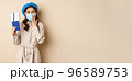 Covid pandemic and travelling concept. Portrait of cute girl in medical face mask going on trip, showing passport with tickets abroad and looking excited, beige background 96589753