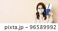 Travel and covid-19 pandemic. Girl in medical face mask travelling, showing passport with two tickets on plane, standing against beige background 96589992