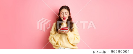 Celebration and holidays. Happy birthday girl lick her lips and look with tempted face at b-day cake, wants to bite, standing against pink background 96590004