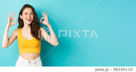 Young carefree woman say yes and nod in approval, showing okay gestures to praise good choice, show perfect body in summer outfit, ready for vacation, standing over blue background 96590110
