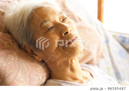 介護ベッドに横たわる認知症の高齢女性 96595487