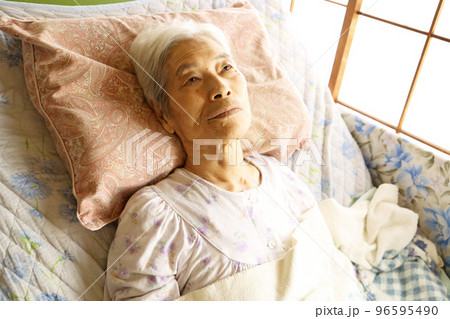 介護ベッドに横たわる認知症の高齢女性 96595490