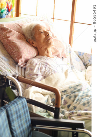 介護ベッドに横たわる認知症の高齢女性 96595491