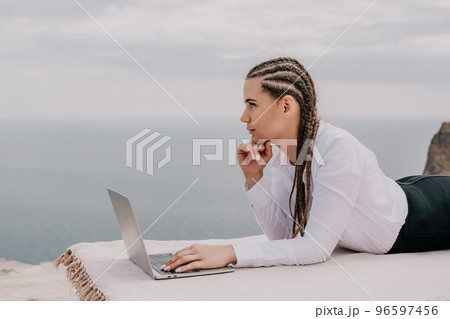 Silhouette of laptop and cup on the beach over sea sunset. Sparkling sea water on background. Freelancer, blogger working on notebook on the beach. 96597456