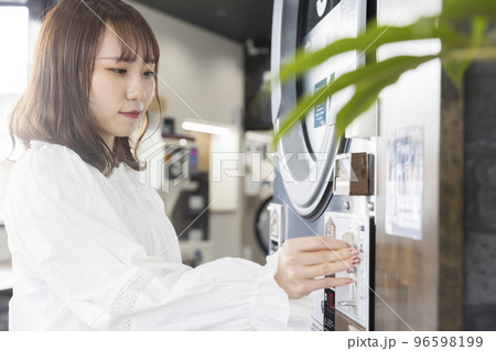 コインランドリーで洗濯をする若い女性　お金を入れる 96598199