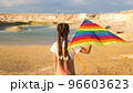 The girl holds a bright kite above her head against the blue sky 96603623