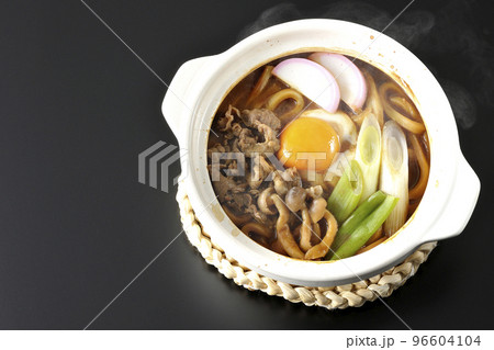 牛肉、しめじ、長葱、カマボコ、卵黄が入っている熱々味噌煮込みうどんを黒背景で俯瞰撮影 96604104