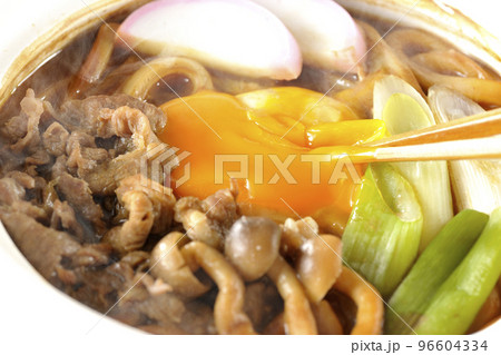 牛肉、しめじ、長葱、カマボコ、卵黄が入っている熱々味噌煮込みうどんの黄身を箸で割る 96604334