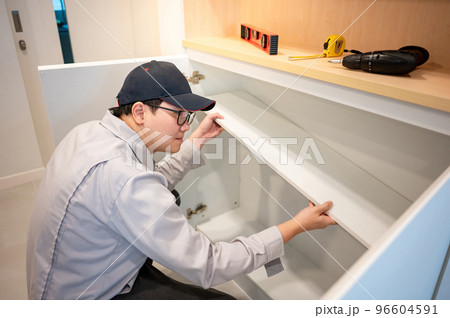Asian male furniture assembler installing cabinet panel 96604591