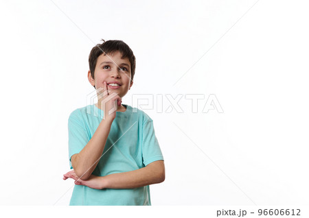 Happy teenage boy wearing turquoise t-shirt, holding his hand at chin and cutely smiling, thoughtfully looking at aside, isolated over white background with copy ad space for promotional text 96606612
