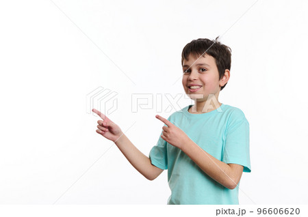 Isolated portrait on white background of a smart school boy, cheerfully smiling teenager wearing blue turquoise t-shirt, looking at you while pointing at advertising space for your promotional text 96606620