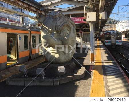 JR高尾駅3・4番線ホームにある石造りの天狗の面と発車を待つ甲府行普通列車と東京行快速電車 96607456