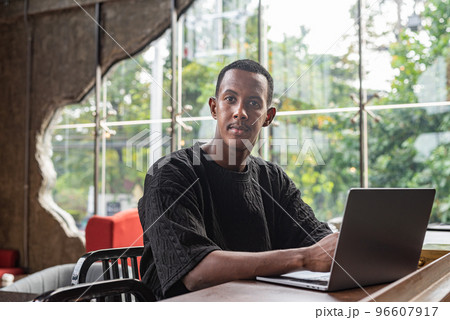 Handsome black man sitting and using laptop computer indoors Handsome black man sitting and using laptop computer indoors 96607917