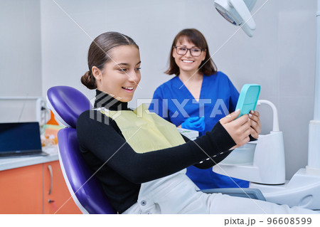 Happy female with mirror sitting in dentist chair looking at healthy teeth 96608599