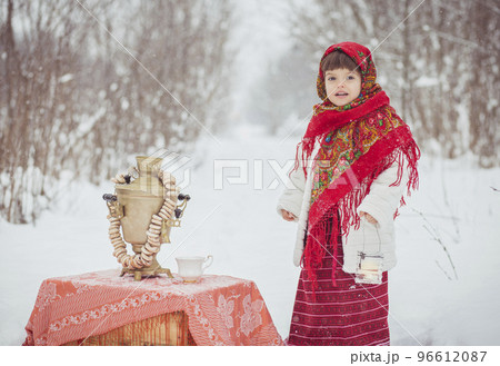 Adorable girl in old clothes in winter forest with samovar and bagels 96612087
