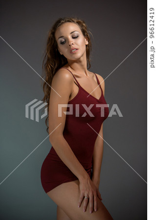 Young beautiful woman in red T-shirt and shorts dancing on a dark gray studio background 96612419