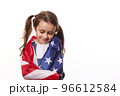 Close-up of delightful little girl with two cute ponytails, hugs herself, covered on United States of America flag, on independence day, isolated over white background, with space for your advertising 96612584