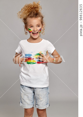 Beautiful little girl with a painted hands and cheeks is posing on a gray background. Beautiful little girl with a painted hands and cheeks is posing on a gray background. 96612635