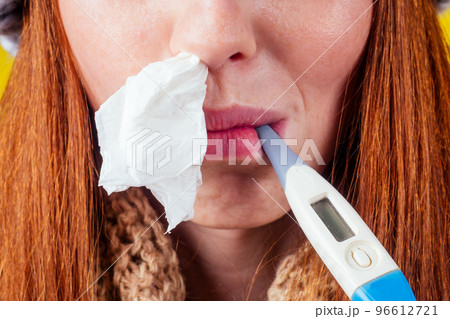 unwell redhaired ginger woman runny nose wearing knitted sweater and scarf with many pills in hand in studio yellow background 96612721