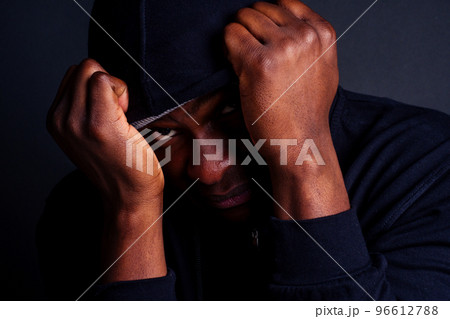 worried young african american mele wearing gray hat and black hoody with hood hiding from the rapist s blow attacker studio black dackground worried young african american mele wearing gray hat and black hoody with hood hiding from the rapist s blow attacker studio black dackground 96612788