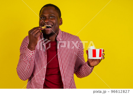 handsome latin man eating fries with appetite and enjoyment in studio yellow background 96612827