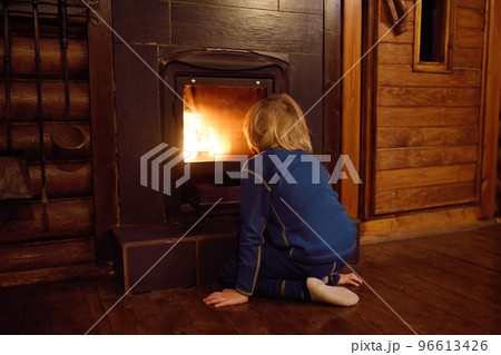 Little child is warming himself by the fireplace after a walk in cold weather in a village house. Preschool boy looks at the flame by the fire place. 96613426