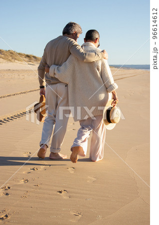 Senior couple walking barefoot on wet sand at seashore 96614612