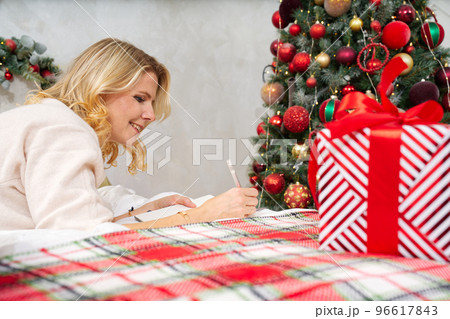 happy woman with pen and notebook making wish list or to do list for new year in bed over christmas tree. xmas holidays concept 96617843