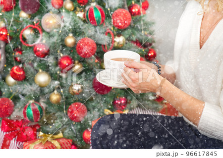 Girl in white sweater holding a cup of warm coffee or tea on background of a Christmas tree. Girl in white sweater holding a cup of warm coffee or tea on background of a Christmas tree. 96617845