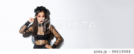 Image of annoyed young woman in halloween gothic dress scolding someone stupid, rolling finger on temple and looking at crazy person, standing over white background 96619988