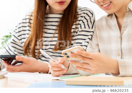 スマホを見ながら勉強をする女子大生二人の手元 スマホを見ながら勉強をする女子大生二人の手元 96620235