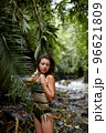 Portrait Young slender girl posing in the jungle hiding behind a palm leaf. Wildlife and a girl 96621809