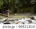 A young, slender girl poses on a tree trunk that has fallen into the river in the middle of a dense jungle 96621810