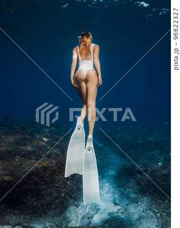 Woman freediver with white fins underwater. Freediving with beautiful girl in deep ocean Woman freediver with white fins underwater. Freediving with beautiful girl in deep ocean 96622327