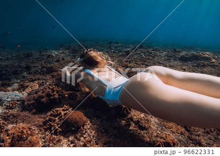 Behind view of woman freediver glides underwater over corals. Freediving in deep blue ocean 96622331