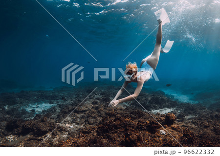 Woman freediver in white swim wear dive with fins over corals. Freediving in tropical blue ocean 96622332