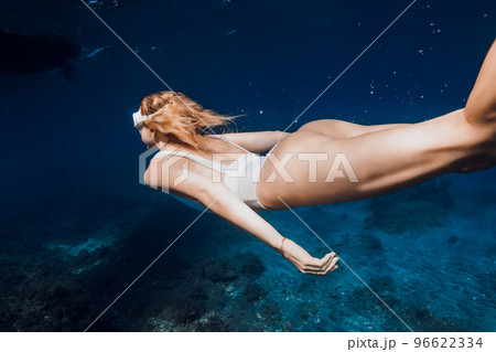 Behind view of woman freediver glides underwater over corals. Freediving in deep blue ocean 96622334