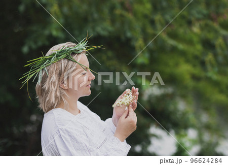 Woman in nightgown with wreath holds elderberry flowers in the forest 96624284
