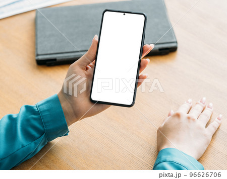 Online conference. Office woman. Digital mockup. Female hands holding smartphone with blank screen sitting desk in light room interior. Online conference. Office woman. Digital mockup. Female hands holding smartphone with blank screen sitting desk in light room interior. 96626706