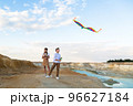 Brother and sister launch a bright big kite into the sky near a flowing river 96627184